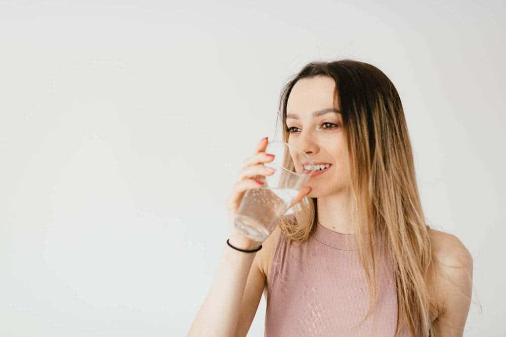 Femme qui boit un verre d'eau avec le sourire